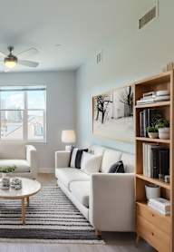 A modern kitchen with a refrigerator, a dining table with chairs, and a living area with a sofa.