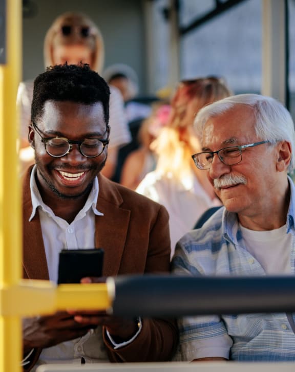 two men sitting on a bus looking at a cell phone