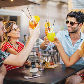 Four people toasting with drinks at a bar.