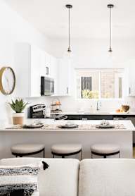 A modern kitchen with a breakfast bar and a white couch with pillows.