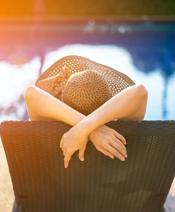 A person wearing a hat is sitting on a chair by the pool.