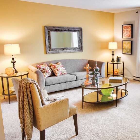 A living room with a grey couch, a yellow chair, and a coffee table at Hummingbird Pointe & The Gardens, Parma, Ohio