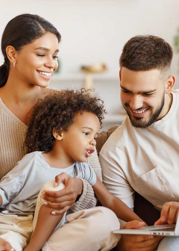 A family of three is sitting on a couch with a laptop.