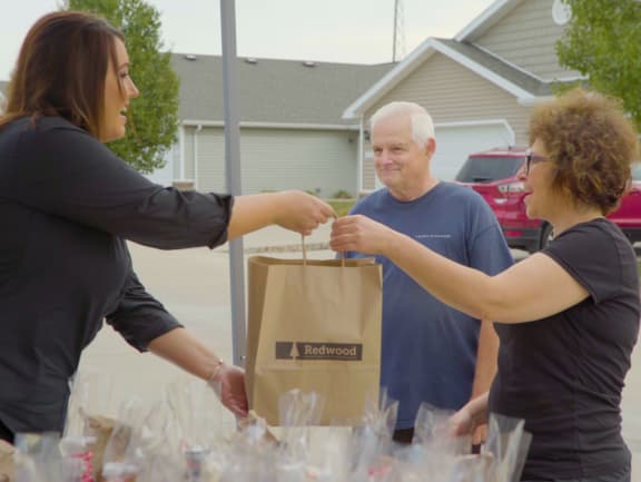 a woman handing a bag of food to an older man and a woman in a black shirt
