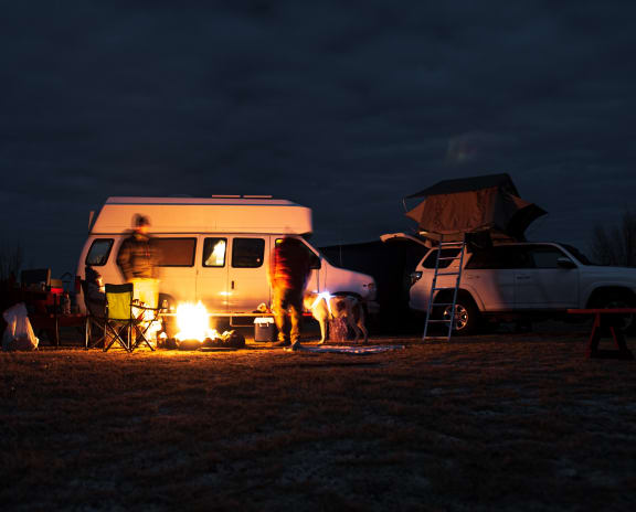 Campers Standing Around Fire in Front of Van and SUV