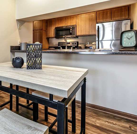 A kitchen with a wooden table and bench, a clock on the wall, and a microwave above the stove.