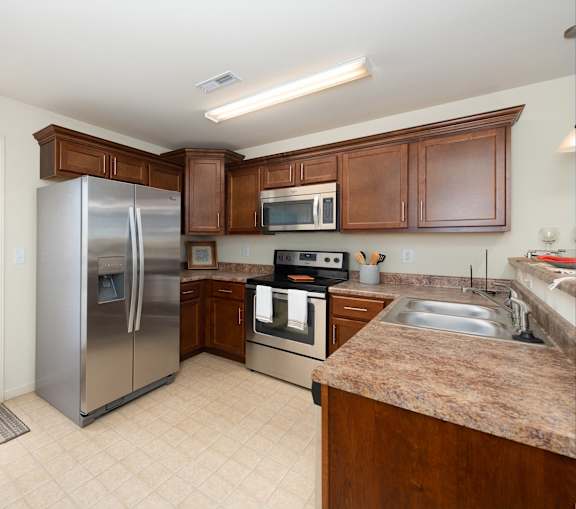 A kitchen with a refrigerator, microwave, oven, sink and cabinets.