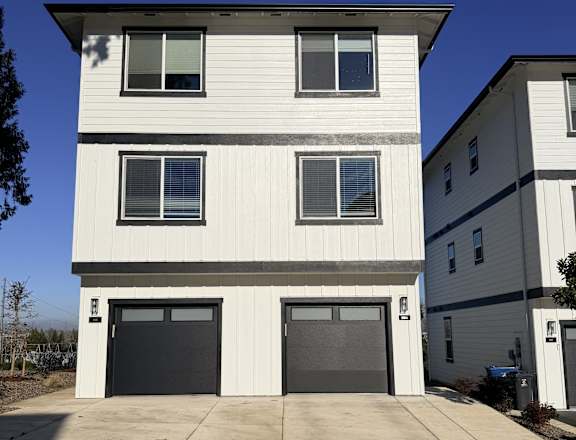 A two-story white house with black garage doors.