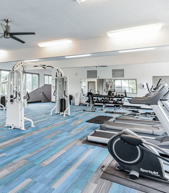 a gym with cardio machines and weights on the floor and windows
