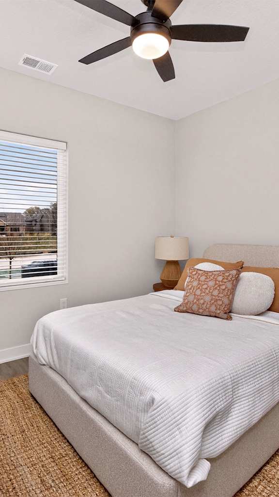 A bedroom with a bed, a ceiling fan, and a window with blinds.