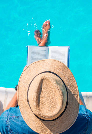 A person is reading a book while sitting by a pool.