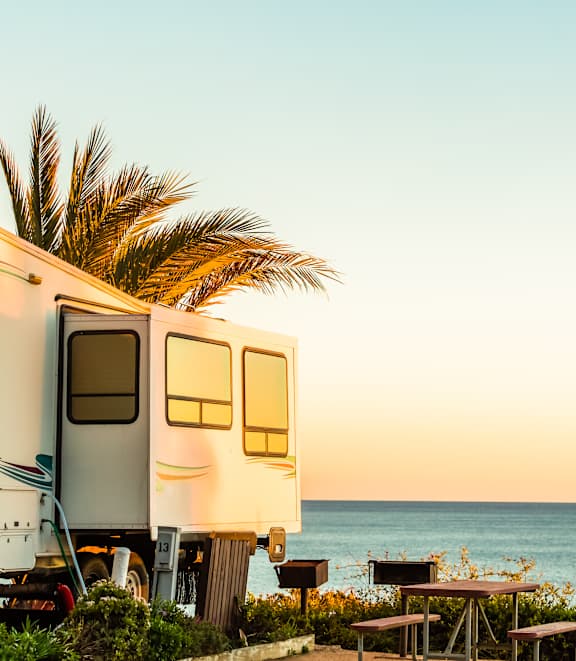 A white RV is parked next to a wooden picnic table on a beach.