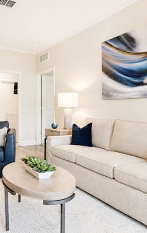 A living room with a white couch, a blue chair, and a painting on the wall.