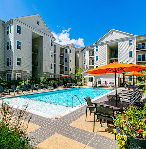 Outdoor pool area with lounge chairs and orange umbrellas at an apartment complex.