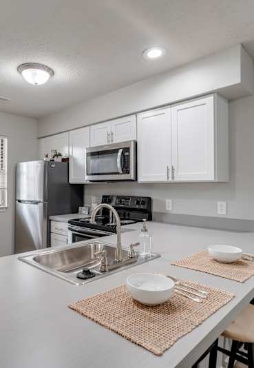 A modern kitchen with a stainless steel refrigerator, microwave, and a sink with a mat on the counter.