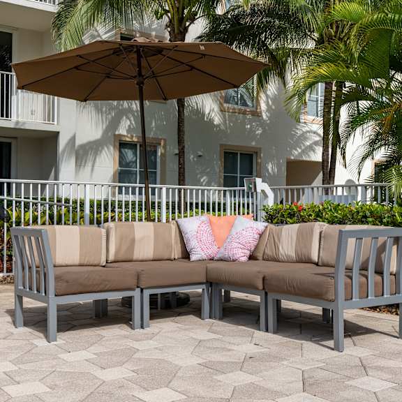 A grey couch with a tan cushion and a tan umbrella on a patio.