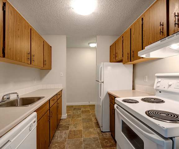 A kitchen with white appliances, light counter, and spacious wooden cabinets at Gateway Gardens. 