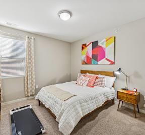 A bedroom with a bed, nightstand, and a painting on the wall.