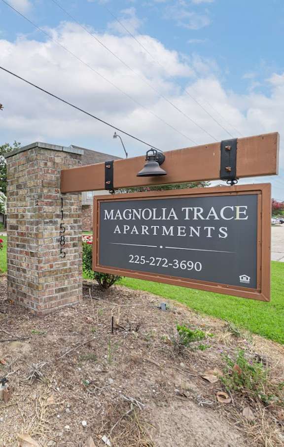 A sign for Magnolia Trace Apartments is displayed in front of a brick wall.