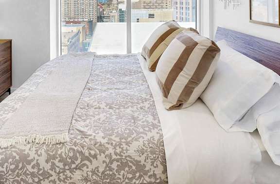A bedroom with a bed, a dresser, and a window overlooking a cityscape.