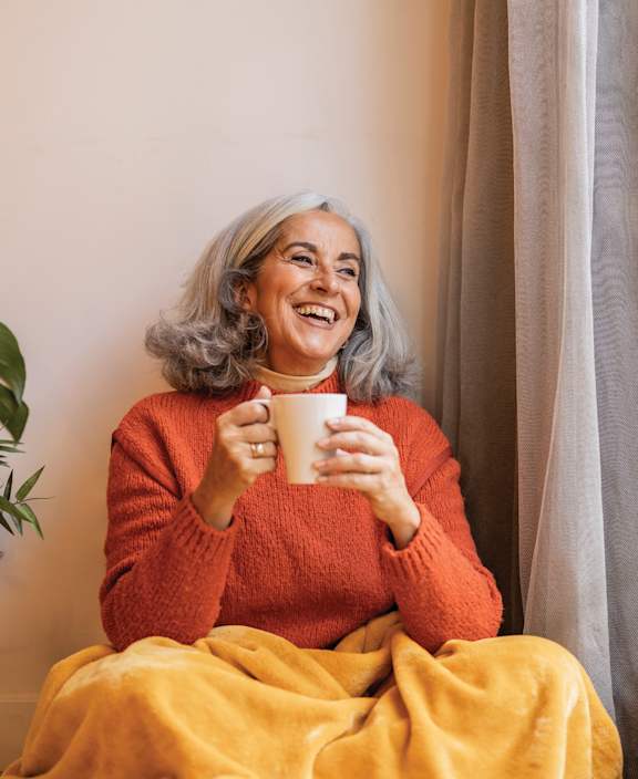 an older woman sitting on a couch holding a cup of coffee at The Carillon, Greensboro, 27455
