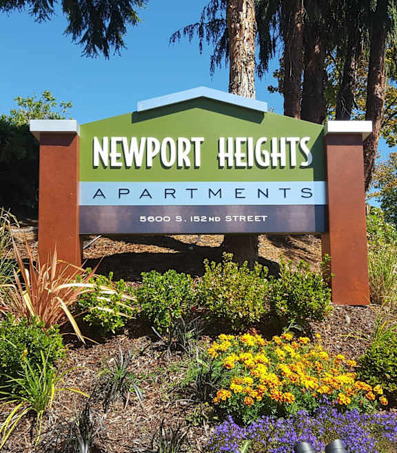 A sign for Newport Heights Apartments is surrounded by plants and flowers.