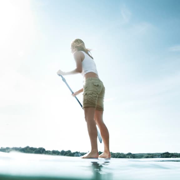 a woman paddle boarding on the water on a sunny day