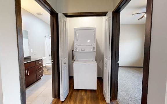 A white washing machine/dryer is in a closet between two rooms.