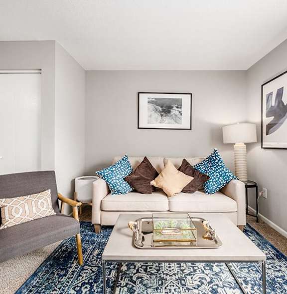 A living room with a grey armchair, a white sofa, and a coffee table with a tray on it.
