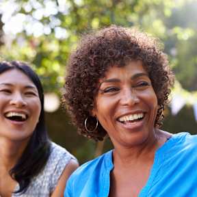 Three people are laughing together in a park.