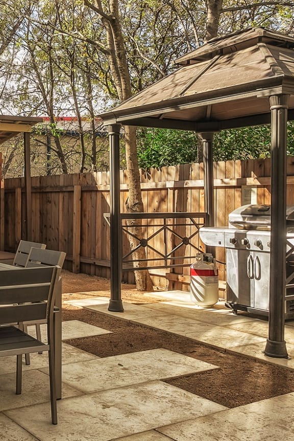 a patio with a table and chairs and a gazebo and a grill