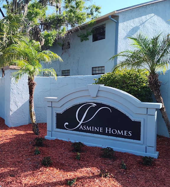 A white sign that says "Jasmine Homes" in front of a house.