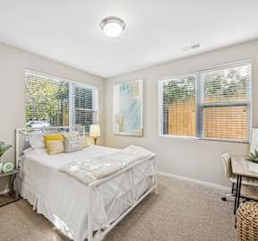 A bedroom with a white bed and a window with blinds.