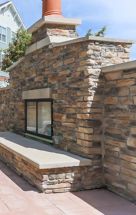 A patio with a stone fireplace and blue chairs.