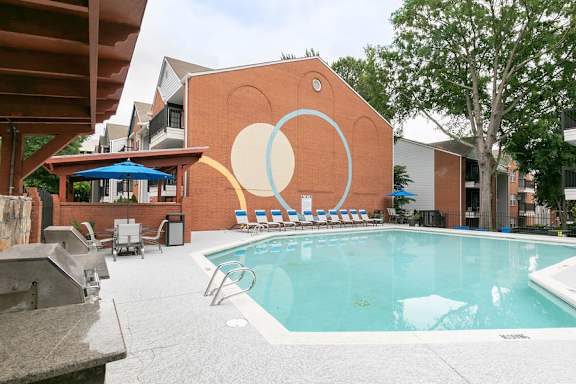 A pool with a blue umbrella and chairs.