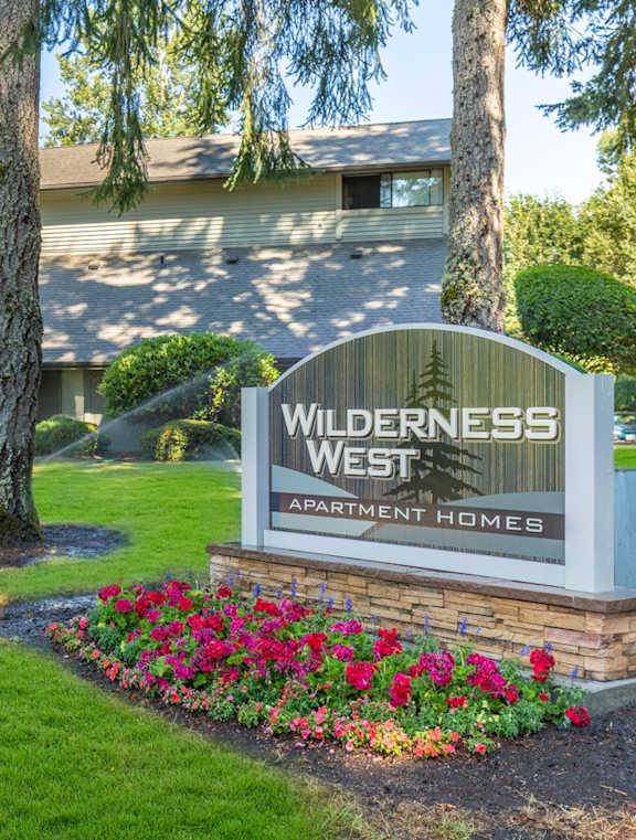 A sign for Wilderness West Apartment Homes is in front of a house.