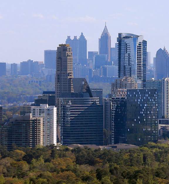 A city skyline with tall buildings and trees in the foreground.