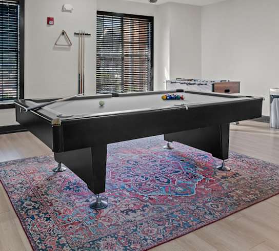 A pool table is in the middle of a room with a rug on the floor.