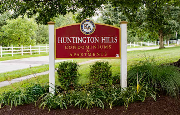 A sign for Huntington Hills Condominiums is in front of a white fence.