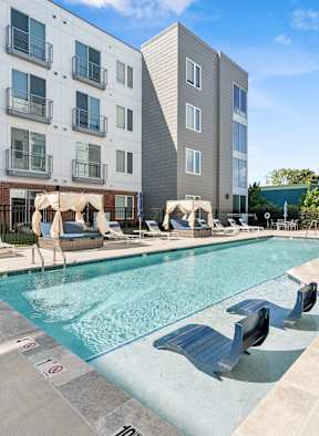 A pool with a slide and sun loungers in front of a building.