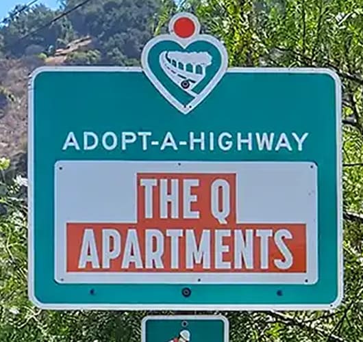A sign for Adopt-A-Highway featuring The Q Apartments.