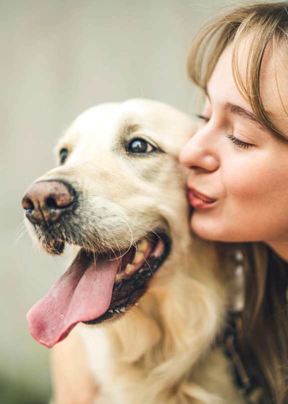 A woman is kissing a happy dog on the cheek.