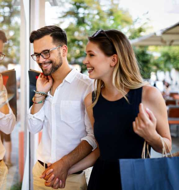 A man and woman are shopping together, holding hands and smiling.