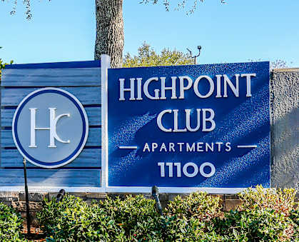 A sign for Highpoint Club Apartments stands in front of a well-manicured hedge and colorful flowers.