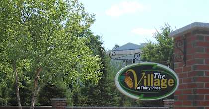 A sign for The Village at Thirty Pines stands in front of a brick wall.
