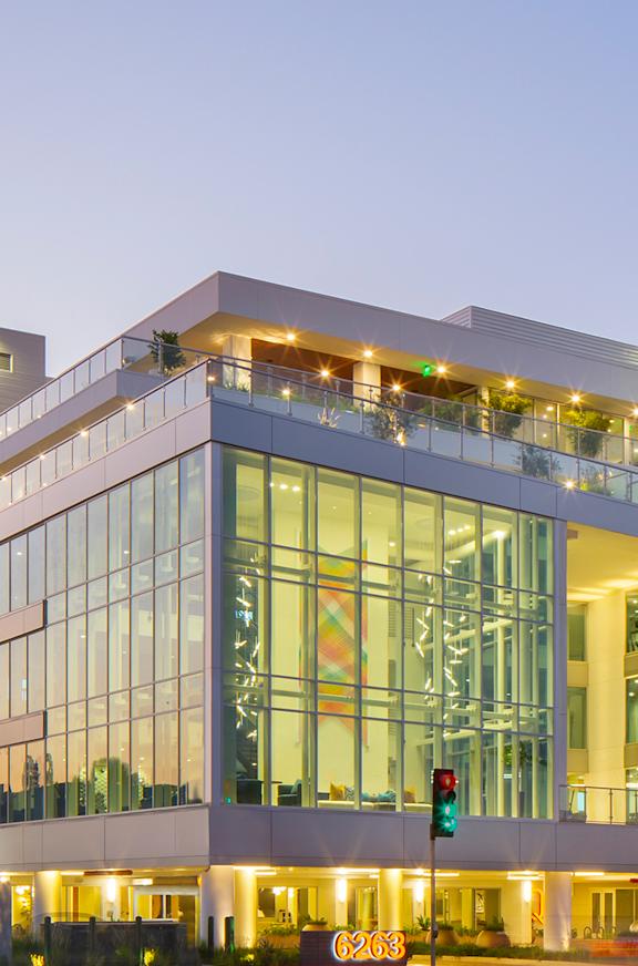 A modern building with a glass facade is illuminated at dusk.