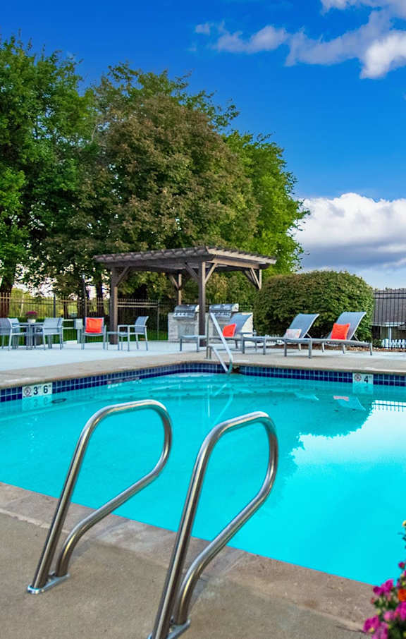 A pool with a diving board and chairs around it.