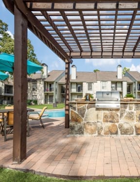 a patio with a stone wall and a grill in front of a house