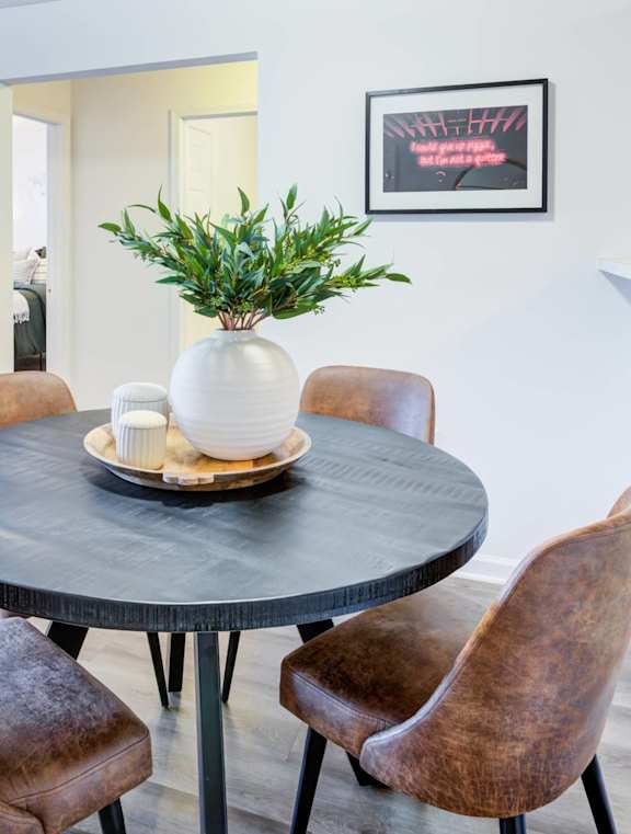 A living room with a grey couch, a round table with a vase on it, and a plant in the corner.