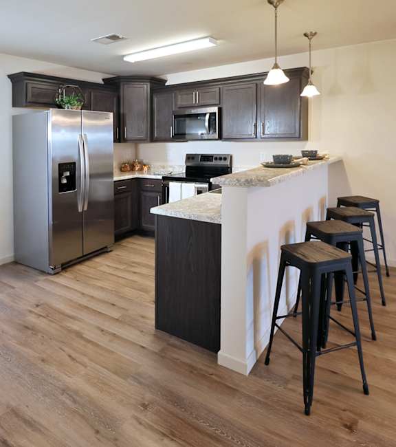 A kitchen with a refrigerator, stove, and bar stools.